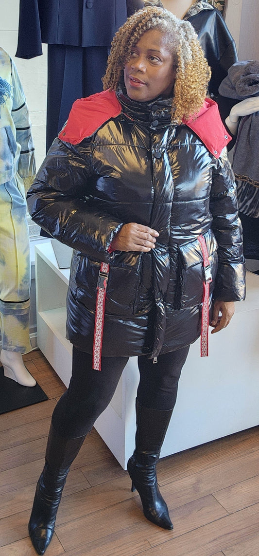 A person standing in a retail environment wearing a sleek black and red puffer coat with a removable hoodie. The coat has a dual-zipper design and the person is also wearing black boots.