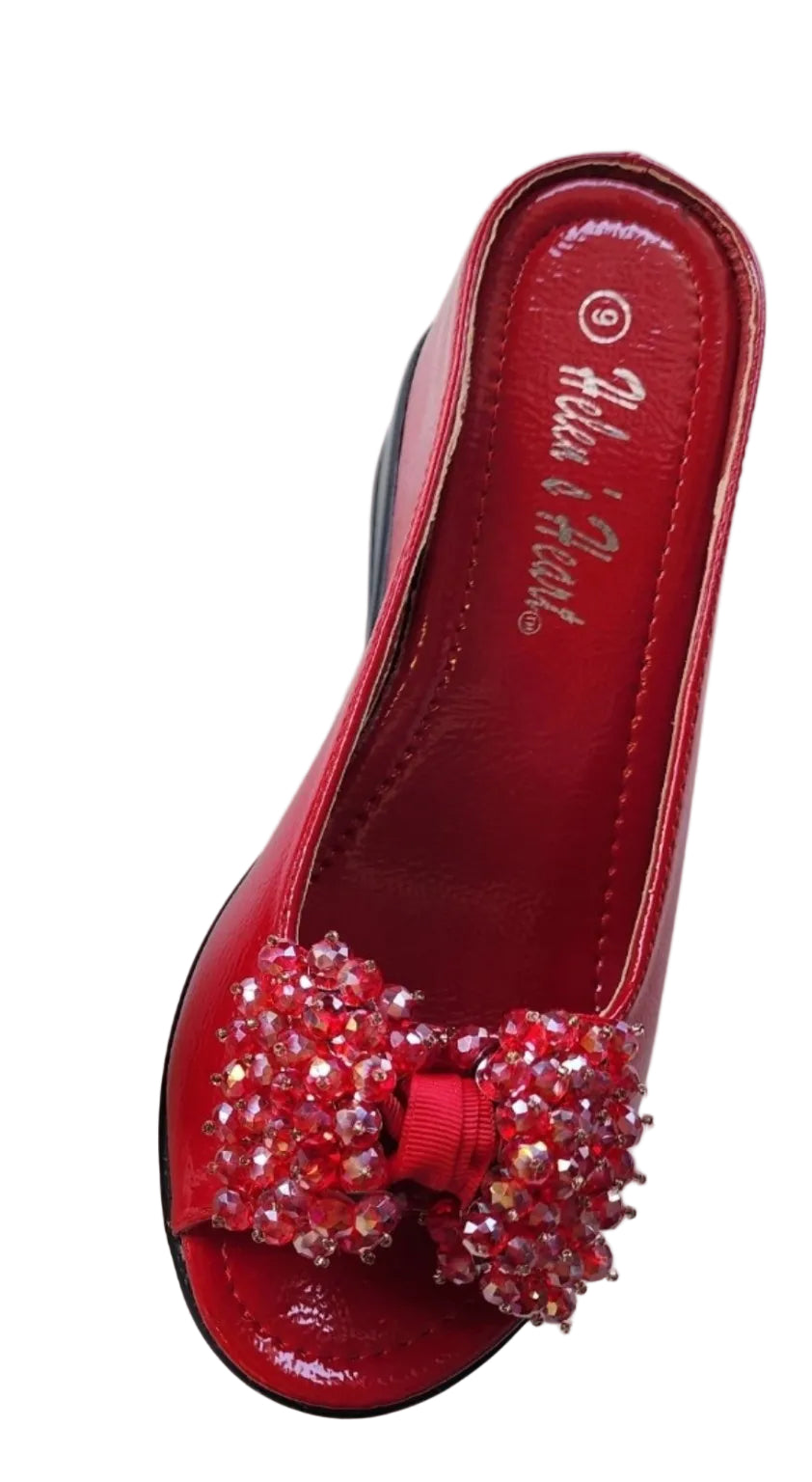 A red peep-toe mule shoe with a large rhinestone-embellished bow on the toe, shown on a plain light background. The insole displays the brand name 'Helen's Heart'.