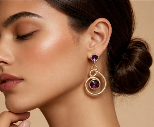 Close-up of a woman wearing gold earrings with purple gemstones against a beige background