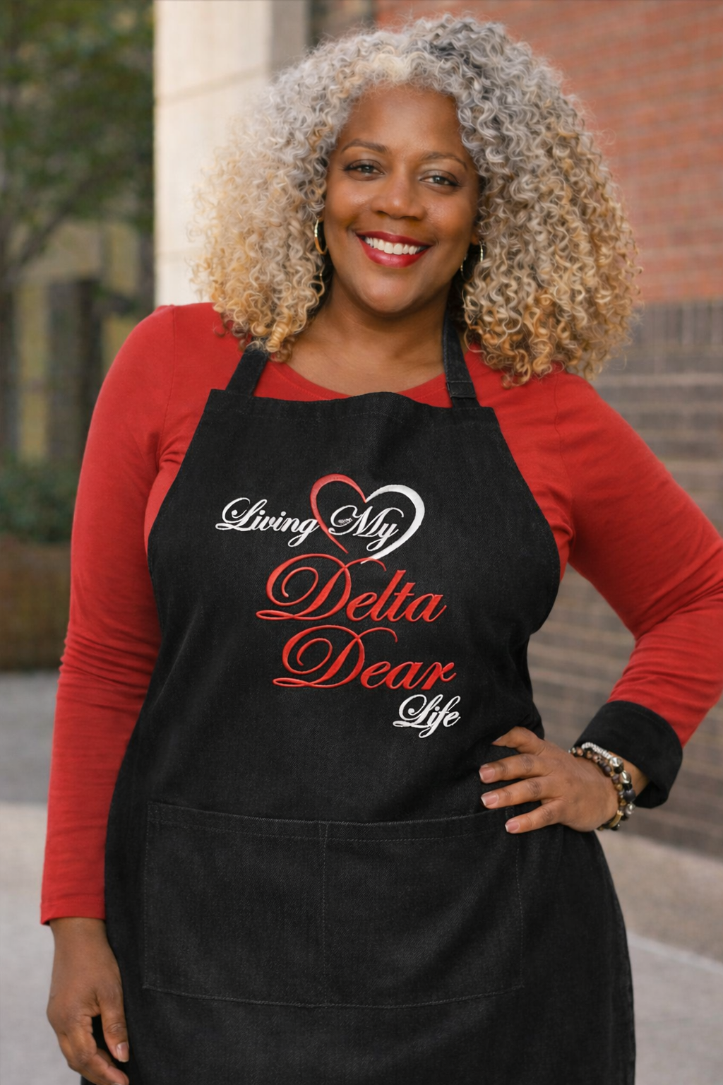 Woman wearing a Black apron with 'Living My Delta Dear Life' text, standing outdoors.