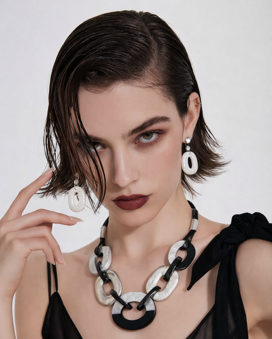 Woman wearing a black and silver necklace with matching earrings on a plain background