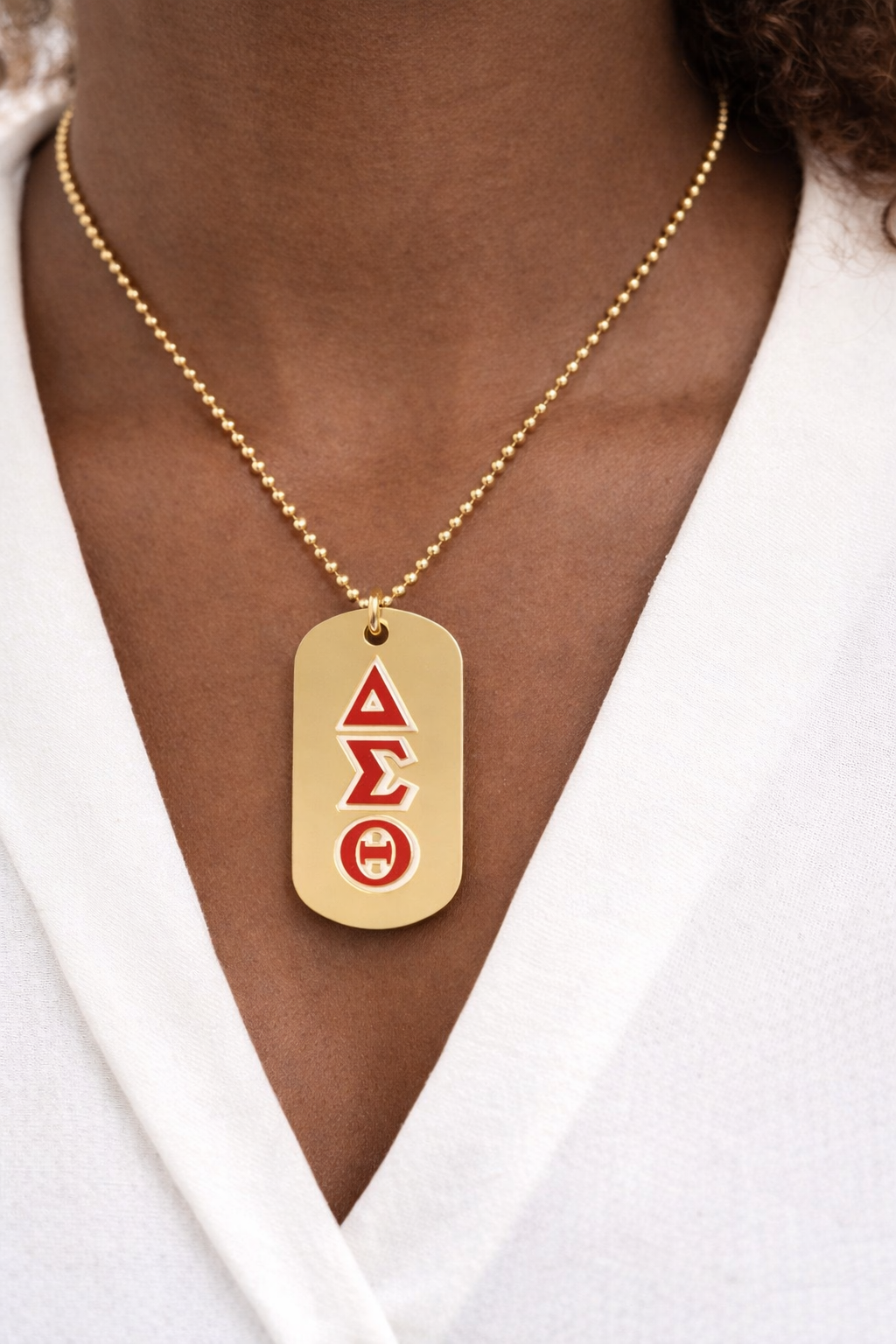 Gold necklace with a pendant featuring symbols on a person wearing a white shirt.