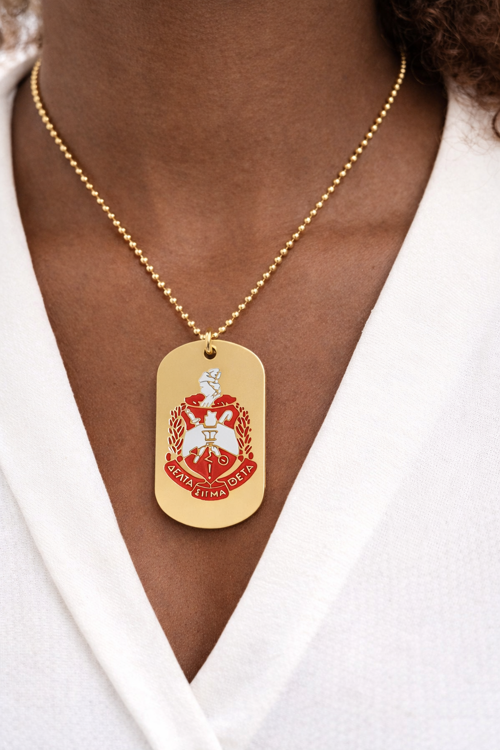 Gold necklace with a red and gold pendant worn by a person against a white background