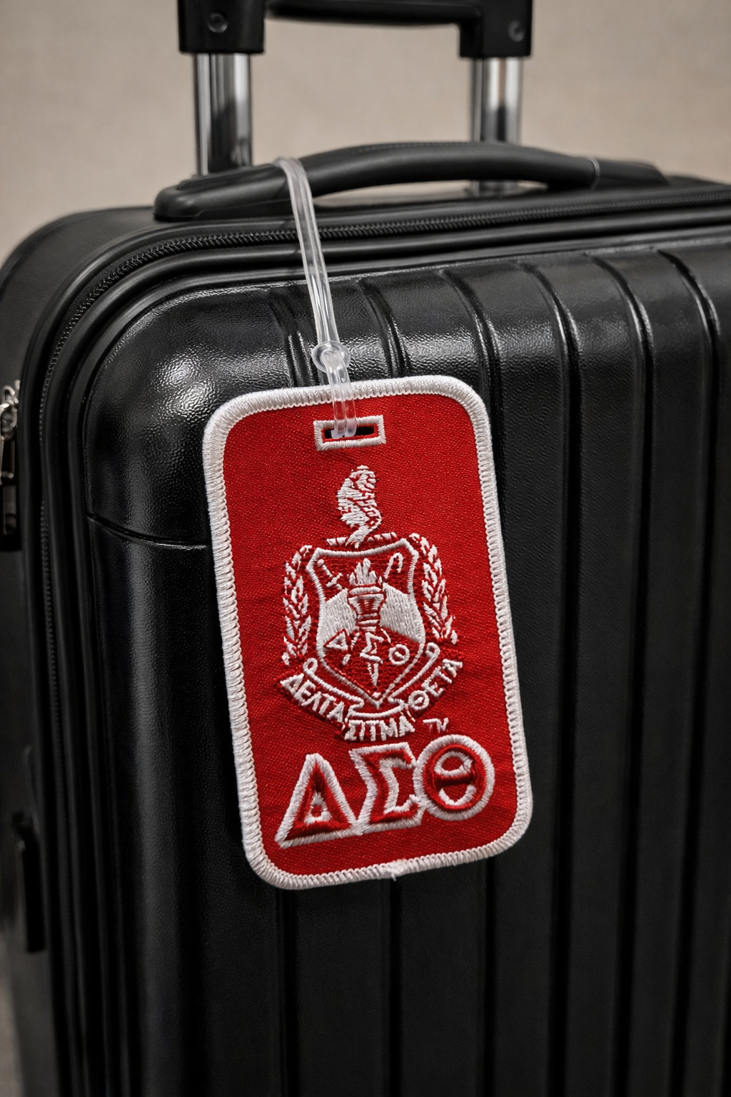 Red and white luggage tag with a Delta logo attached to a black suitcase.
