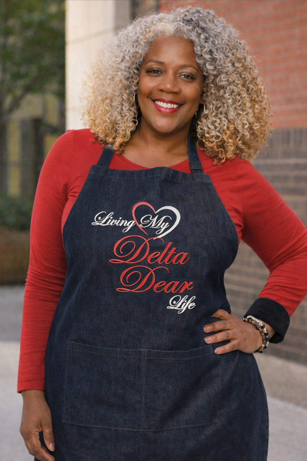 Woman wearing a Denim apron with 'Living My Delta Dear Life' text, standing outdoors.