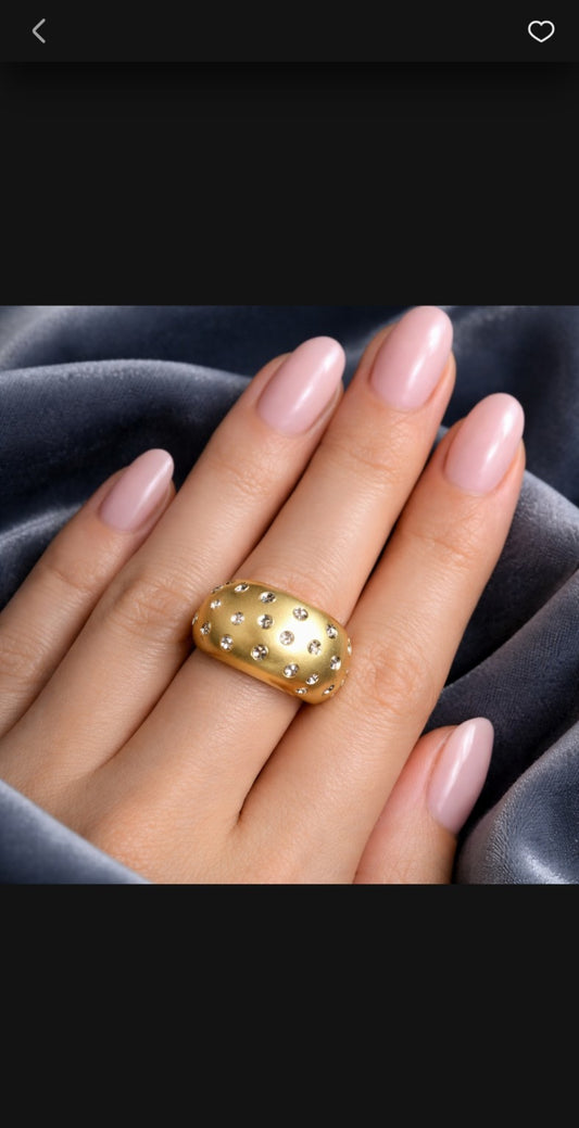 Gold ring on a hand with pink nail polish against a dark background