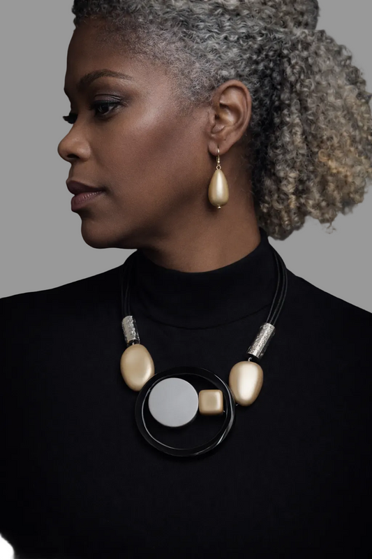 Woman wearing a black turtleneck and a unique necklace and earring set with gold and silver elements on a white background