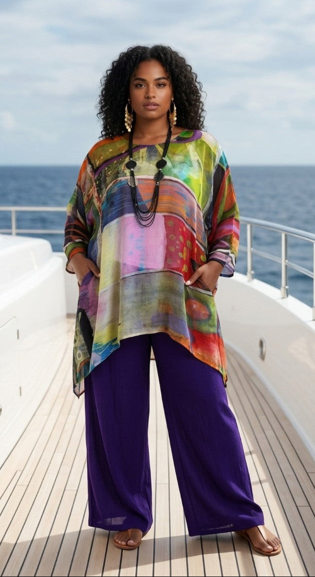 Woman standing on a boat deck wearing a colorful top and purple pants with a scenic ocean background.