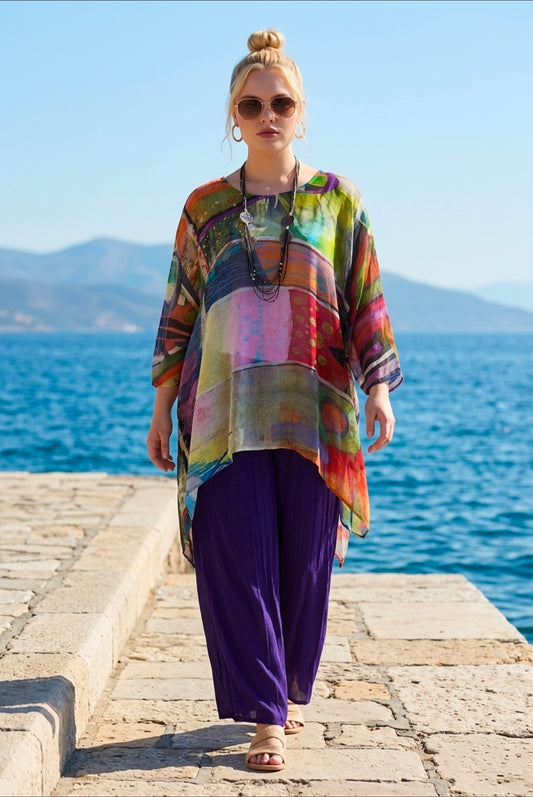 Woman wearing a colorful shirt and purple pants standing on a stone pathway by the sea.